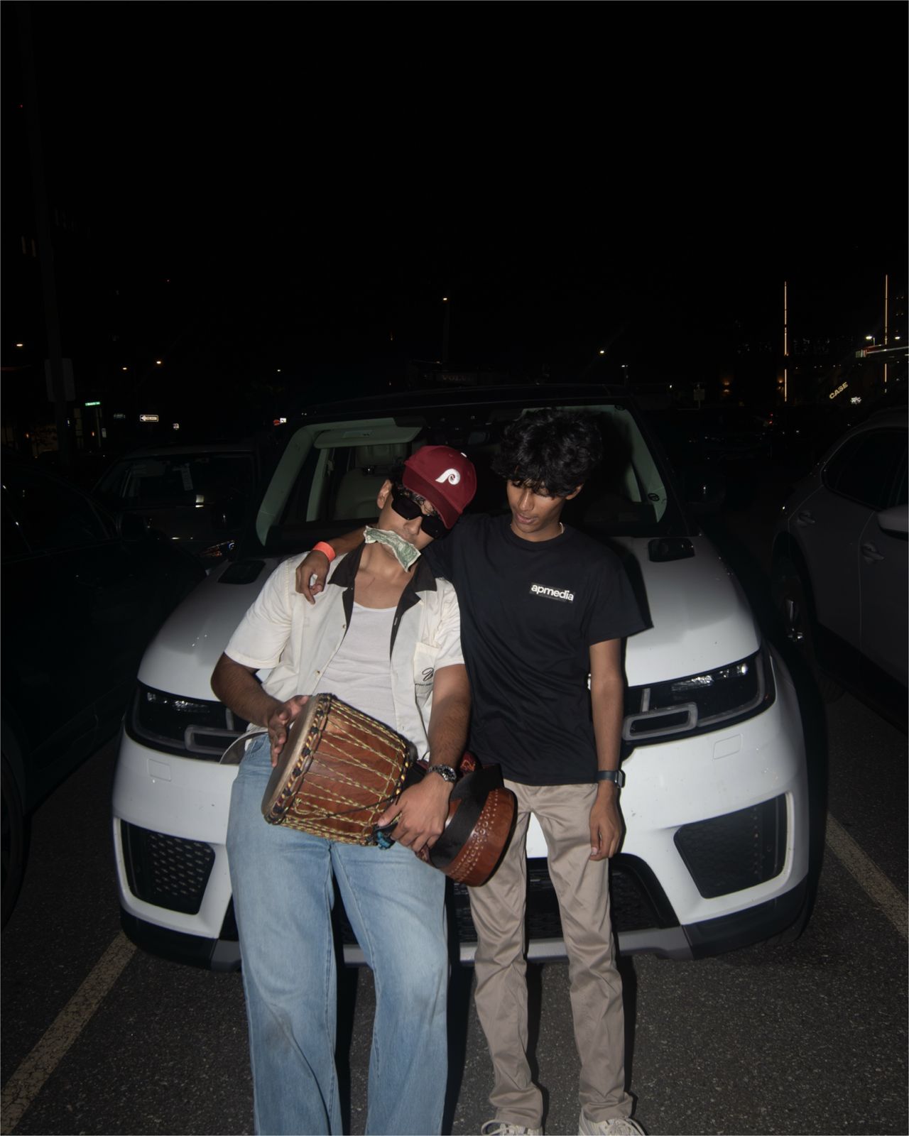 AADIKTIV holding a hand drum in front of a white SUV at night